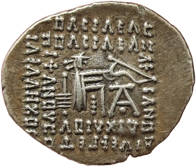 Eine antike Münze mit eingravierter Schrift und einem Bild, das eine Figur darstellt. Die Schrift beinhaltet Symbole und Zahlen, die für historische oder kulturelle Bedeutung stehen könnten. Die Details der Münze sind von archäologischem Interesse.