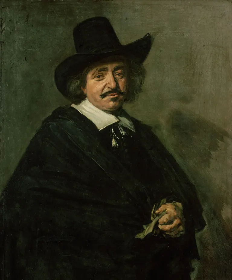 Porträt eines Mannes mit einem großen schwarzen Hut und einem dunklen Umhang. Er hat einen gepflegten Schnurrbart und schaut direkt zum Betrachter. Die Stimmung des Bildes ist ernst und nachdenklich, mit einem neutralen Hintergrund.