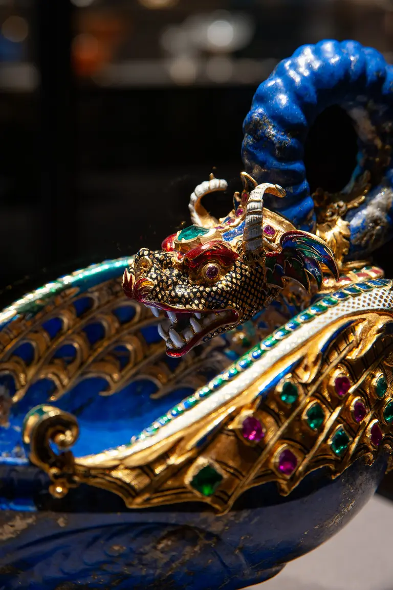 Eine kunstvoll gestaltete Schale in Blau mit einem Drachenkopf, der mit bunten Edelsteinen verziert ist. Der Drache hat geschwungene Hörner und zeigt Zähne. Die Schale ist reich verziert und strahlt durch die glänzenden Farben und Details hohe Handwerkskunst aus.